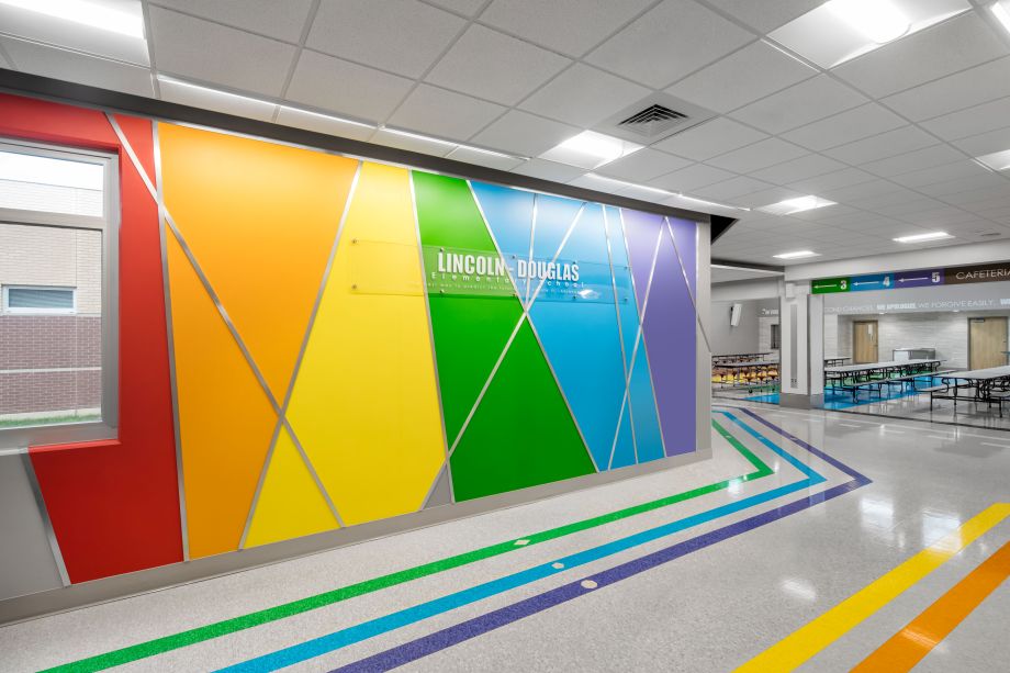 Lincoln Douglas elementary school area with a colorful wall and seating area; flooring design uses wayfinding to help students navigate